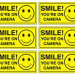 (Set of 6) Smile You’re On Camera Sign – 2″ x 4″ – 4 Mil Vinyl – LAMINATED For Ultimate Protection & Durability – Self Adhesive Decal – UV Protected & Weatherproof – Heavy Duty